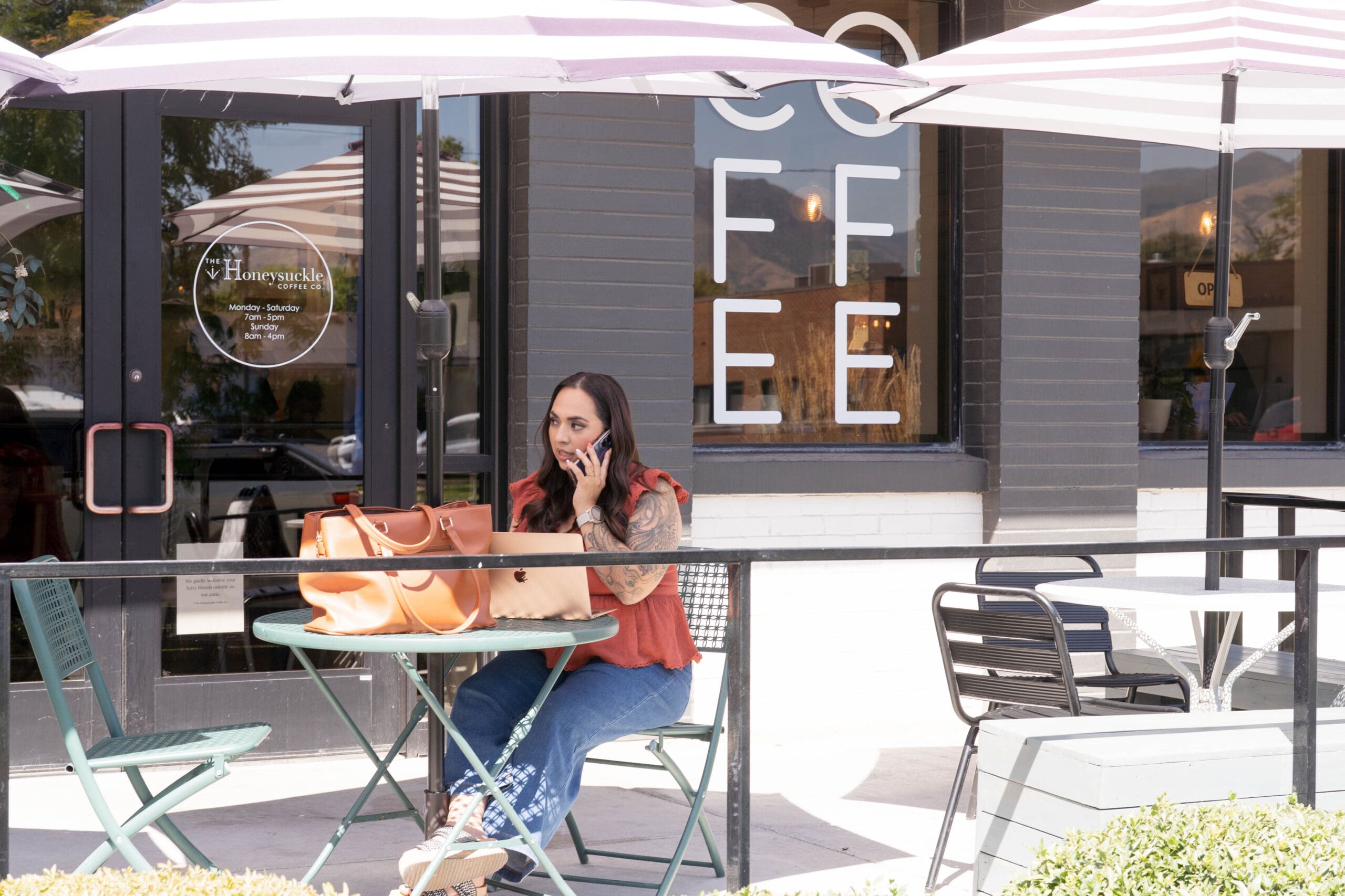 Steph on a phone at a table outside at a coffee shop