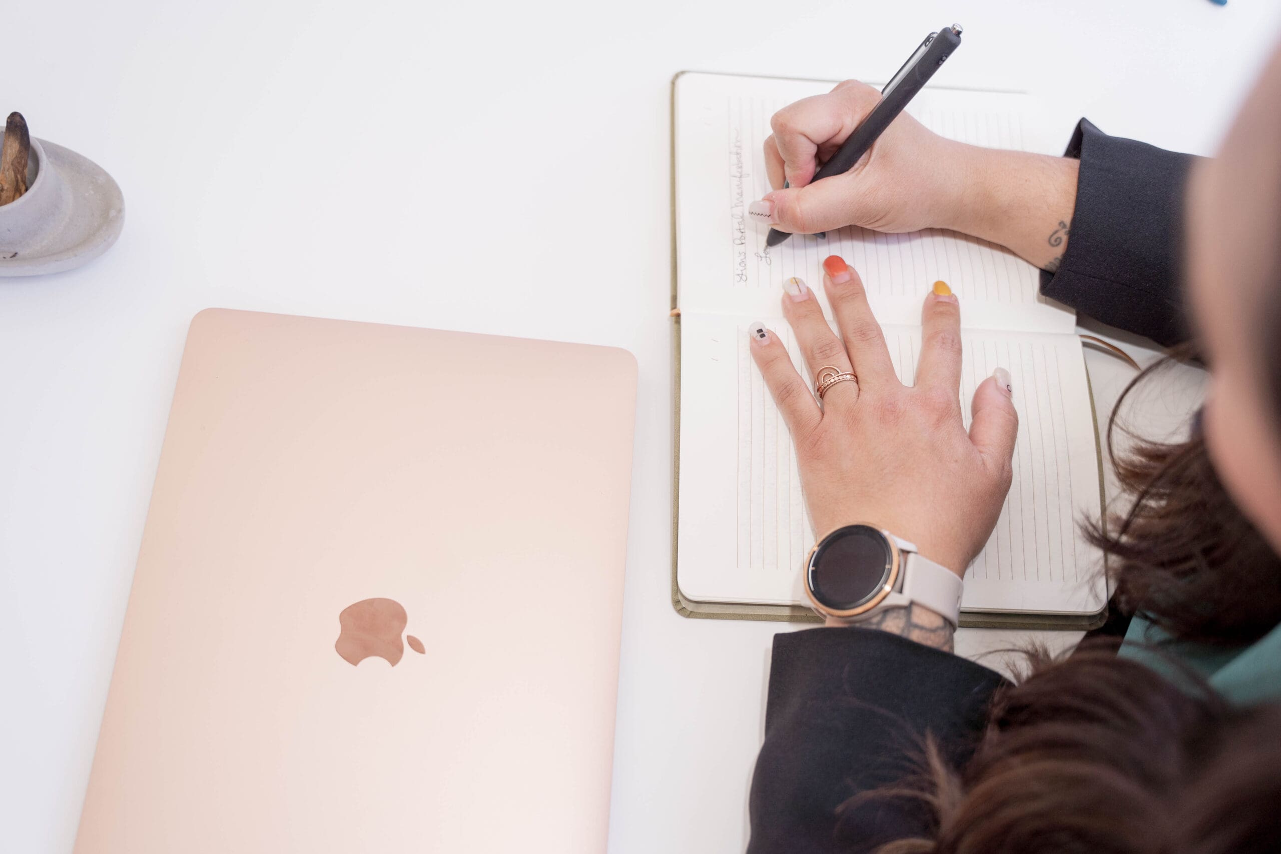 an overhead view of a woman writing in a notebook with a closed laptop near by